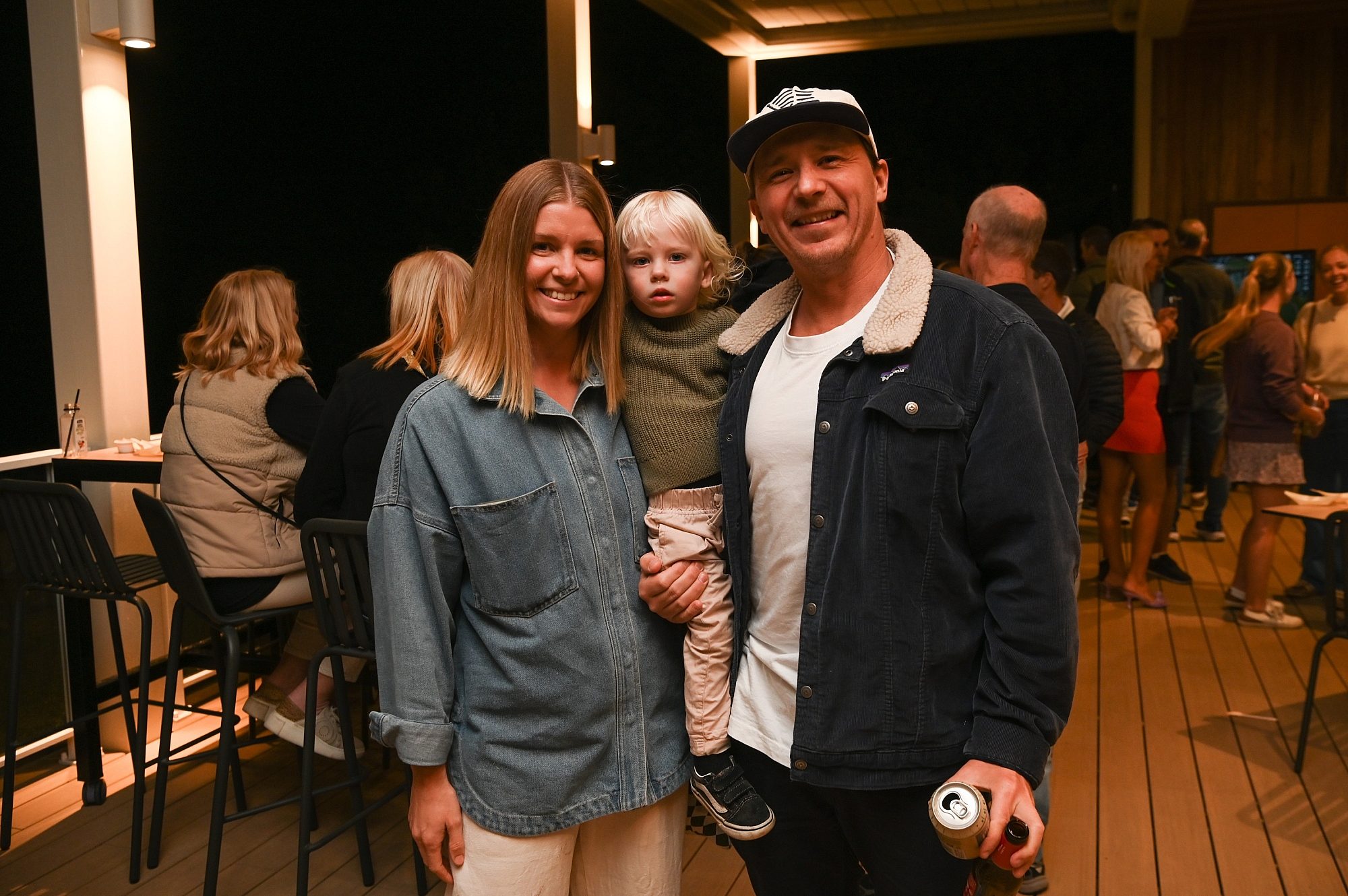 A young couple and child smile at the camera on an outdoor deck.