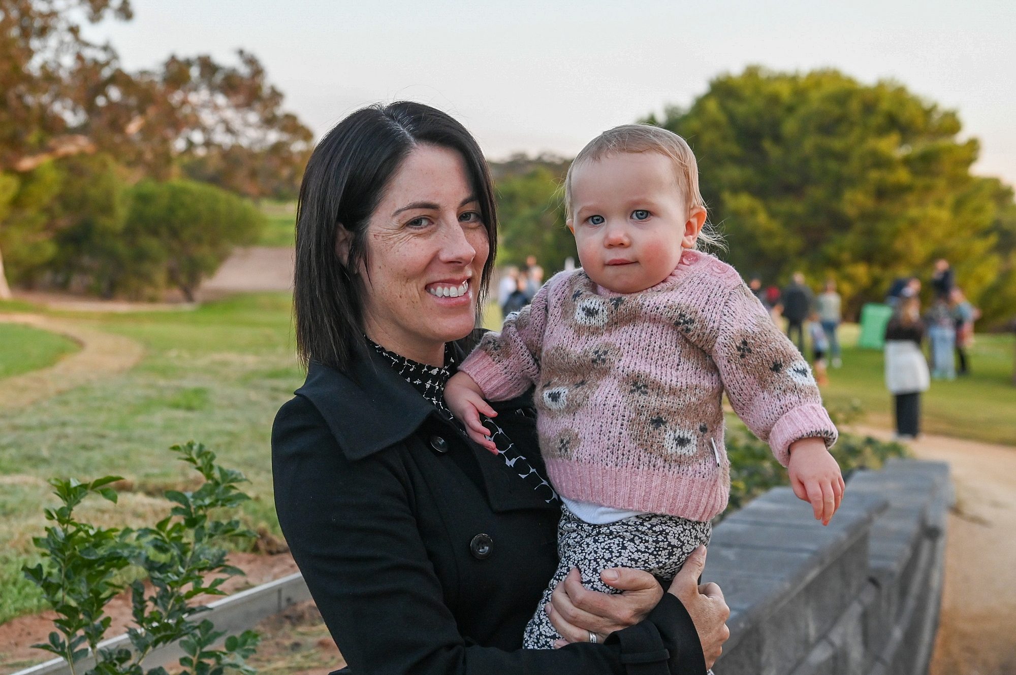 A woman holds a baby, both smiling at the camera.