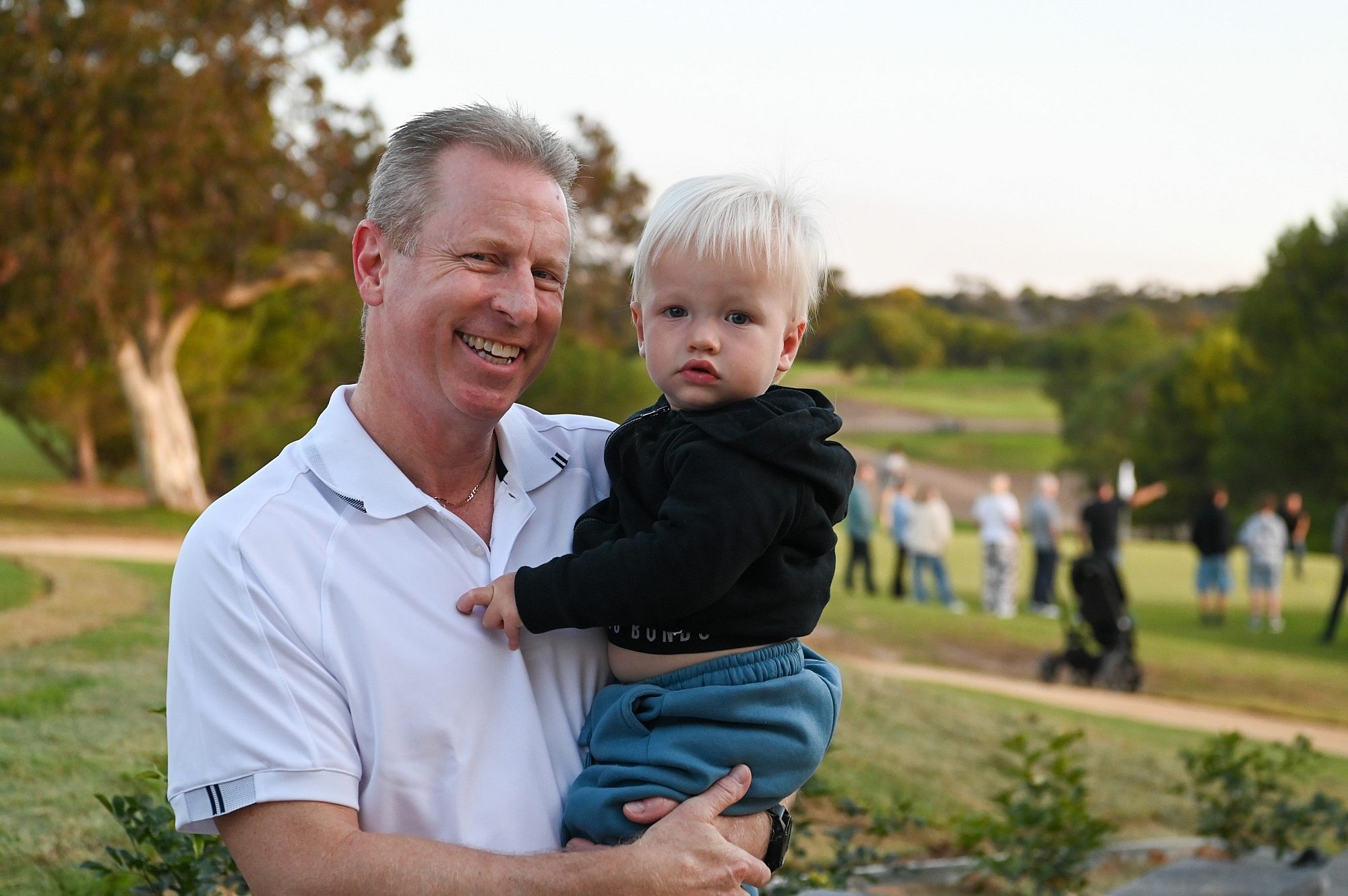 A man holds a baby, both smiling and looking at the camera.