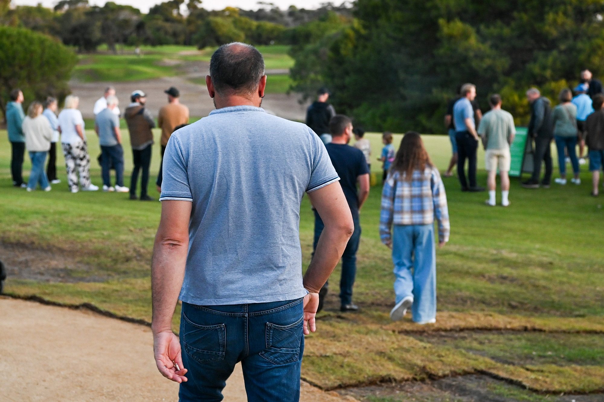 A man in a blue t-shirt is walking towards a crowded golf course.