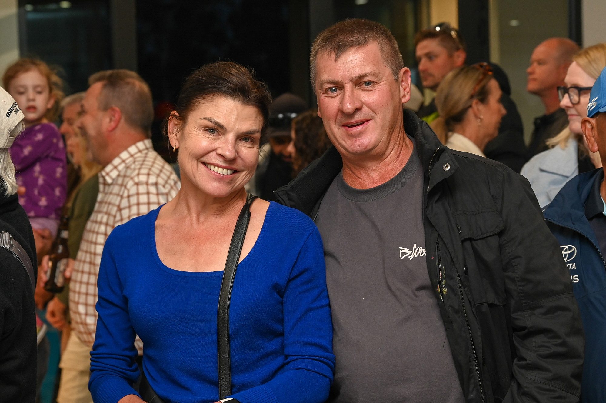 A women in a blue top, and man in grey t-shirt and jacket smile at the camera.