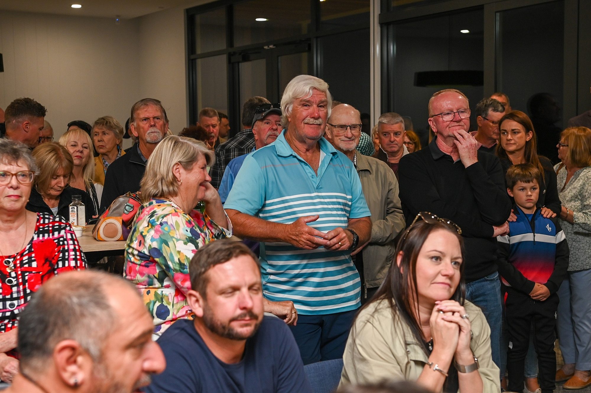 A crowded room full of people all face towards the front of the room.