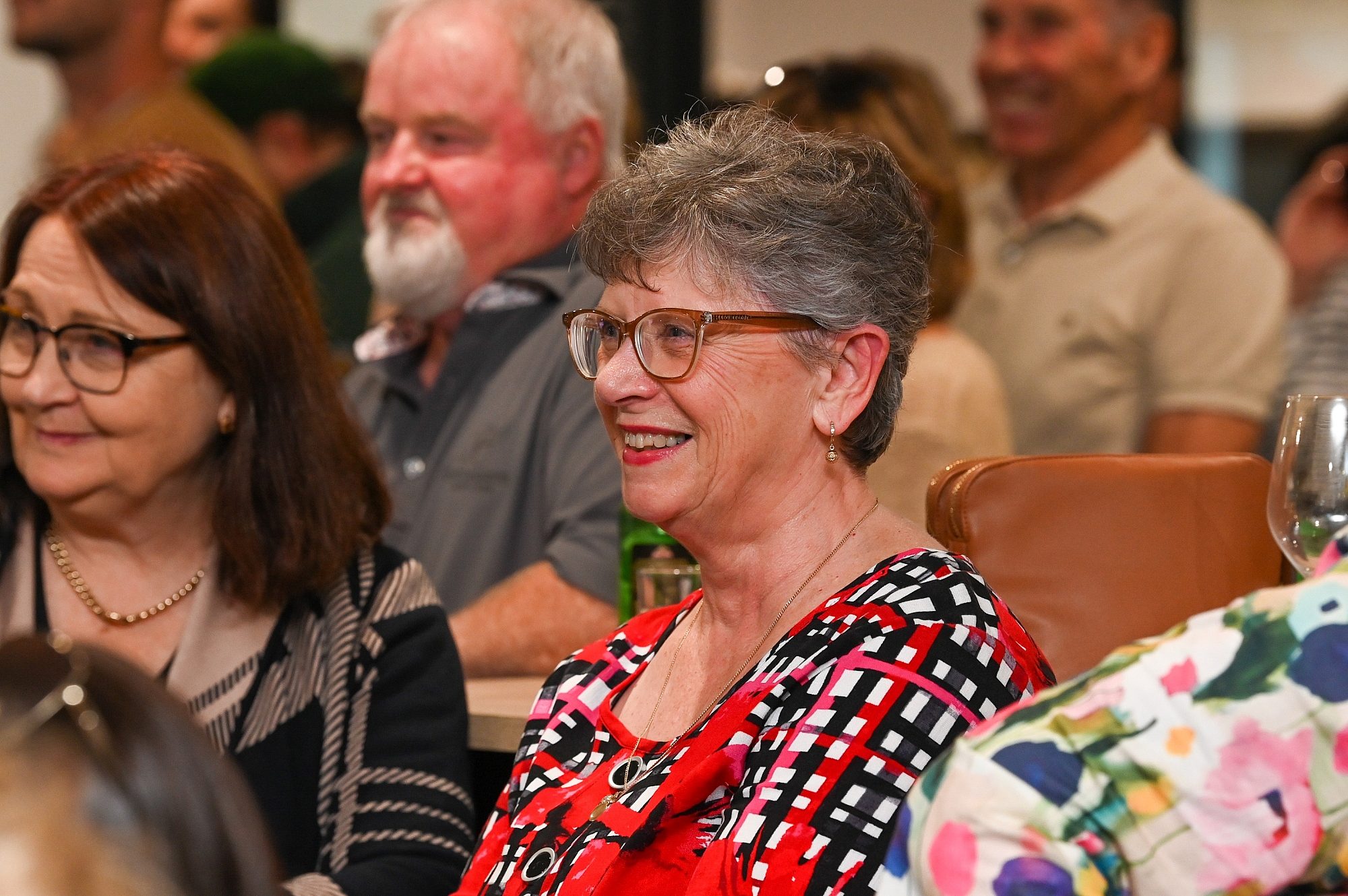 Smiling lady in a red and black check top and glasses smile and looking to the left.
